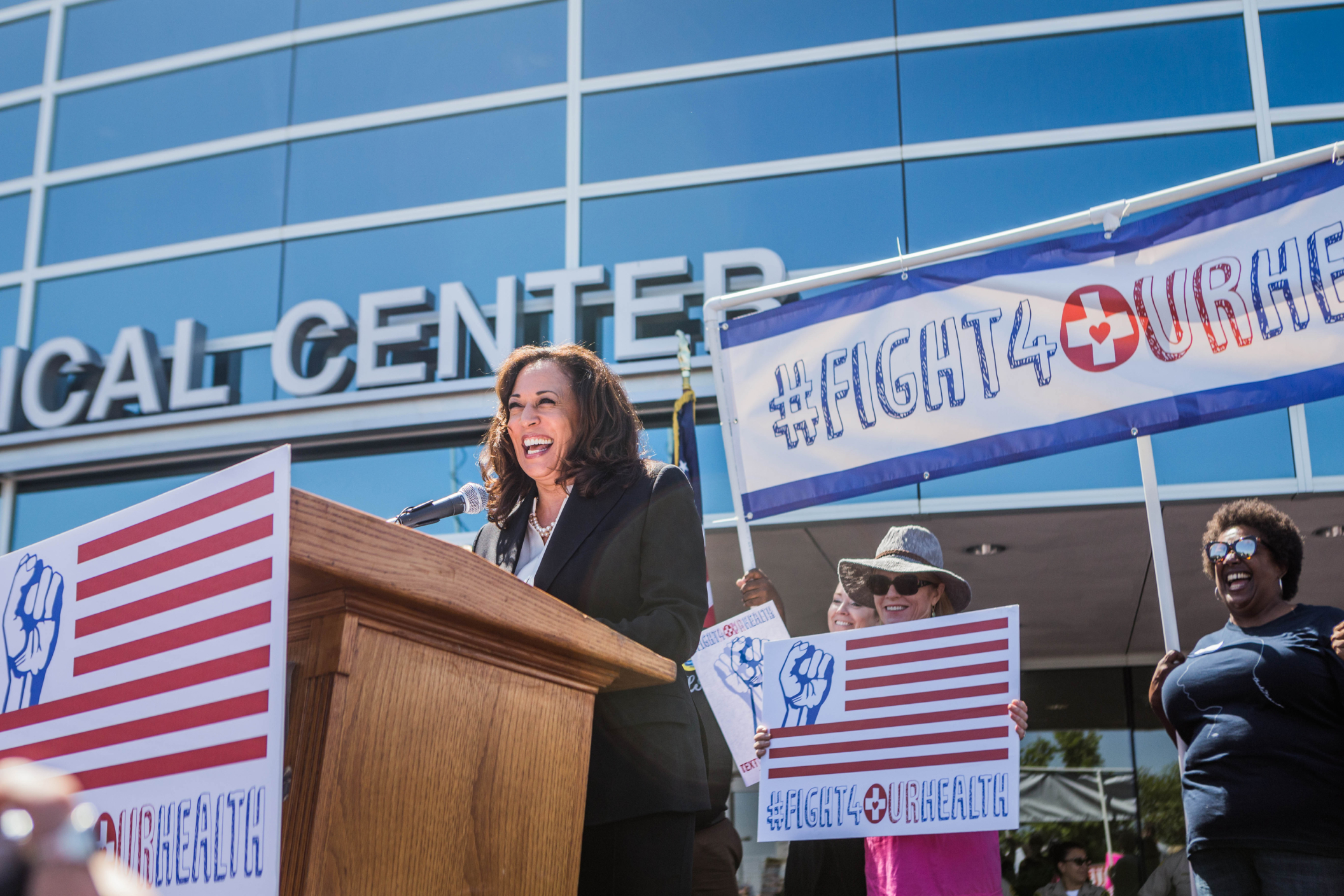 Vice President Harris addressing an audience with signs that say "#Fight4UrHealth"